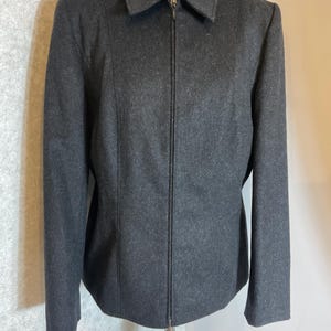 May include: A dark grey jacket featuring a collared neckline and a full-length zip. The jacket has a tailored fit with vertical seams and long sleeves. The garment is displayed on a white mannequin.
