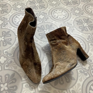 May include: A pair of brown suede ankle boots with a snakeskin pattern. The boots have a pointed toe and a block heel.