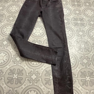 May include: Dark gray, slim-fit pants with a snakeskin pattern. The pants have a classic five-pocket design and a button and zipper closure. The fabric has a subtle sheen, and the overall look is sleek and modern.