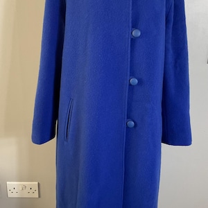 May include: A long, royal blue coat with a classic design. The coat features a notched collar, three large matching buttons, and a single pocket. The coat is displayed on a mannequin.