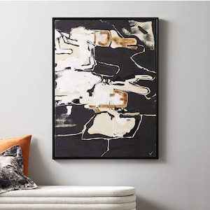May include: Abstract art piece in a black frame. The artwork features a bold composition of black, white, and beige shapes with gold accents. The painting has a modern aesthetic, suitable for home decor.