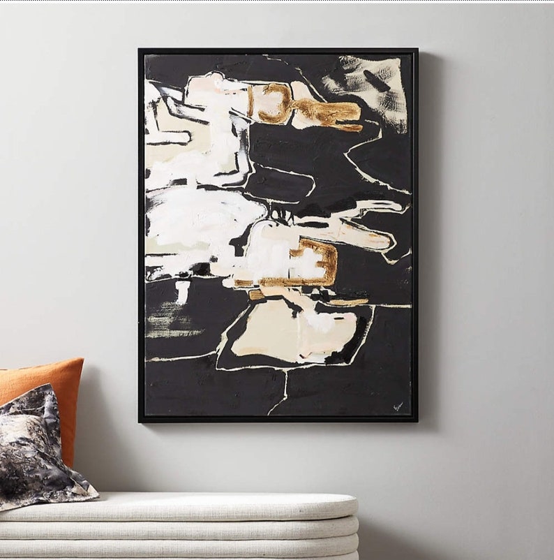 May include: Abstract art piece in a black frame. The artwork features a bold composition of black, white, and beige shapes with gold accents. The painting has a modern aesthetic, suitable for home decor.
