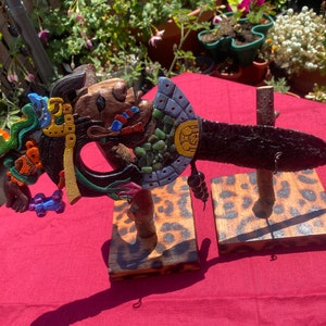 May include: Two carved wooden ceremonial knives with intricate designs. The blades are dark, and the handles feature colorful details, including blue, green, yellow, and orange accents. They are displayed on wooden stands with a leopard print pattern.