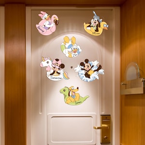 May include: A collection of colorful Disney character decals, including Daisy Duck on a pink flamingo float, Goofy with a snorkel in a yellow duck float, Donald Duck, Mickey Mouse, Pluto on a green dinosaur, and Minnie Mouse on a unicorn float. Each decal has a name.