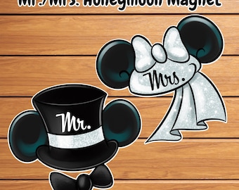 May include: A pair of honeymoon magnets with a Mickey Mouse theme. One magnet features a black top hat with "Mr." written on it, and a bow tie. The other magnet has a white bow and veil with "Mrs." written on it.