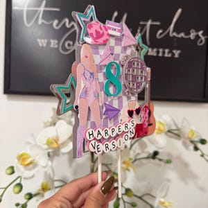 May include: A multi-layered cake topper with a pop star theme. The topper features a figure in a pink outfit, a disco ball, a guitar, and the text "HARPER'S VERSION". Accents include stars, a cassette tape, and the number 8.