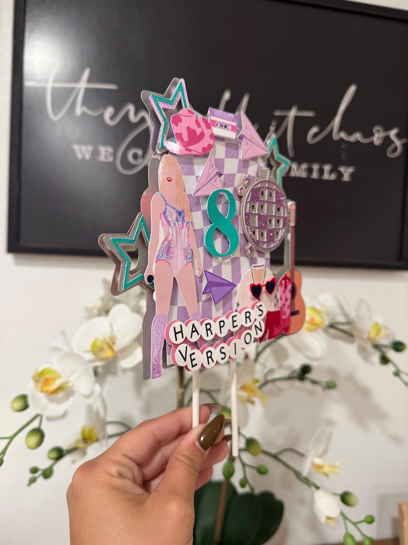 May include: A multi-layered cake topper with a pop star theme. The topper features a figure in a pink outfit, a disco ball, a guitar, and the text "HARPER'S VERSION". Accents include stars, a cassette tape, and the number 8.