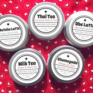 May include: Five silver tins of natural soy wax melts with different flavors: Matcha Latte, Thai Tea, Ube Latte, Milk Tea, and Chamoyada. Each tin has a black and white label with the flavor name and a description of the scent.
