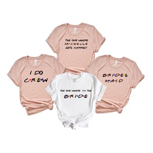 May include: Four t-shirts, three in a light pink and one in white. The shirts have text in a colorful font. The text on the pink shirts reads: "THE ONE WHERE MICHELLE GETS MARRIED", "I DO CREW", and "BRIDES MAID". The white shirt says "THE ONE WHERE I'M THE BRIDE".