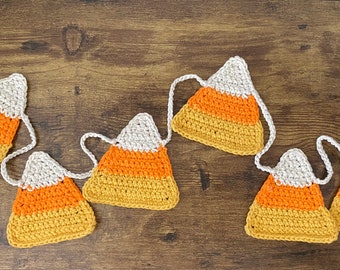May include: A handmade crochet garland featuring candy corn shapes. Each candy corn is crafted with white, orange, and yellow yarn, strung together with a white crochet cord. Perfect for Halloween or fall decor.