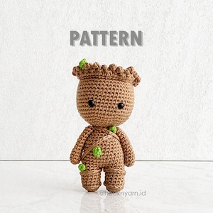 Könnte beinhalten: Häkelmuster für eine braune und grüne Groot-Amigurumi-Puppe. Die Puppe hat einen runden Kopf mit schwarzen Augen und einem kleinen Mund. Die Puppe steht auf einer weißen Oberfläche. Der Text "PATTERN" ist in grauen Buchstaben über der Puppe geschrieben.