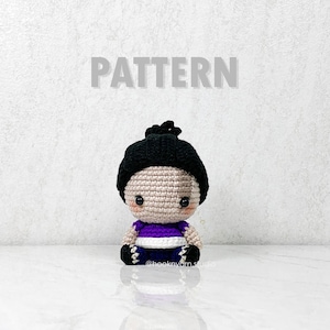 Pode incluir: Uma boneca de crochê feita à mão com um chapéu preto, uma blusa roxa e branca e calções azuis. A boneca tem um tom de pele neutro e olhos grandes e escuros. A palavra "PATTERN" é exibida acima da boneca.