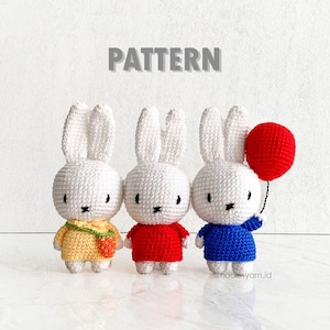 May include: Three handmade crochet bunny dolls. The bunnies are white with black eyes and a black stitched mouth. One bunny wears a yellow dress, one a red shirt, and the third a blue shirt and holds a red balloon. The word "PATTERN" is above the bunnies.