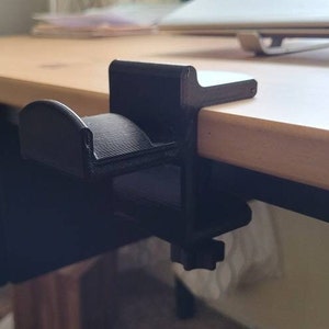 May include: A black plastic desk organizer with a curved hook for hanging items. The organizer is mounted to the edge of a wooden desk.