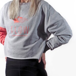May include: A gray and coral cropped sweatshirt with the word "FLOW" and the text "FLOWERS GROW ON WAVES" printed on the front.