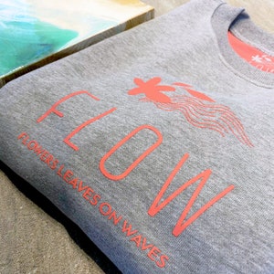 May include: Gray sweatshirt with a coral pink graphic design that says "FLOW" with the words "FLOWERS LEAVES ON WAVES" underneath.