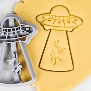 Op de afbeelding: Een grijze plastic koekjesvormer in de vorm van een UFO met aliens erin. De vormer ligt op een gele koekdeeg.