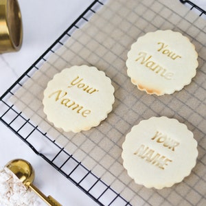 May include: Three plain sugar cookies on a wire rack with parchment paper. Each cookie has the words "Your Name" imprinted on the top.