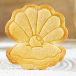 Op de afbeelding: Een lichtgele suikerkoek in de vorm van een schelp met een parel erin.