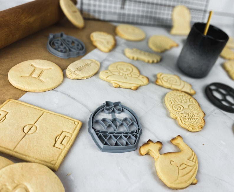 Puede incluir: Un conjunto de cortadores de galletas en diferentes formas, incluyendo una pelota de f&uacute;tbol, una cesta, una calavera, una flor y un par de gemelos. Los cortadores de galletas est&aacute;n hechos de metal y tienen un acabado plateado.