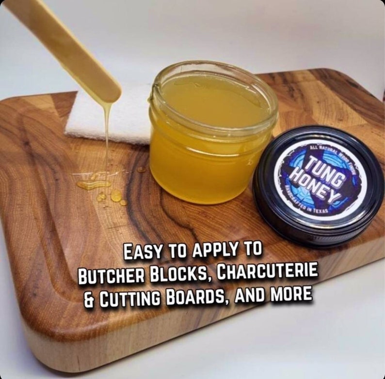 May include: A clear glass jar filled with a yellow liquid, labeled "TUNG HONEY" with a blue and white logo. The jar is sitting on a wooden cutting board with a wooden stick dripping the liquid onto the board. The text "EASY TO APPLY TO BUTCHER BLOCKS, CHARCUTERIE & CUTTING BOARDS, AND MORE" is written below the jar.