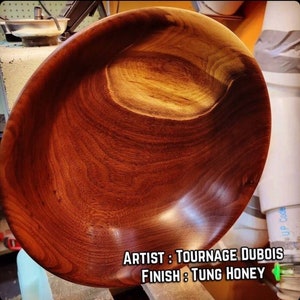 May include: A large, wooden bowl with a rich, reddish-brown color. The bowl has a smooth, polished finish and is made from a single piece of wood. The text "ARTIST: TOURANGE DUBOIS FINISH: TUNG HONEY" is visible at the bottom of the image.