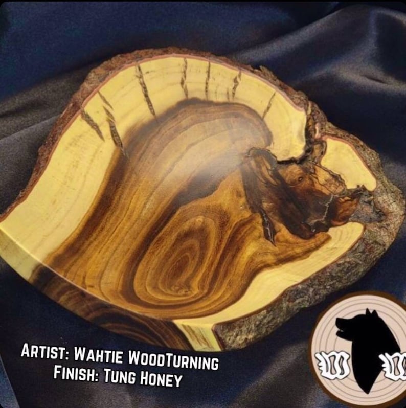 May include: A wooden bowl with a natural edge and a dark brown and light yellow wood grain pattern. The bowl is finished with Tung oil. The artist's name, Wahtie Woodturning, is written below the bowl.