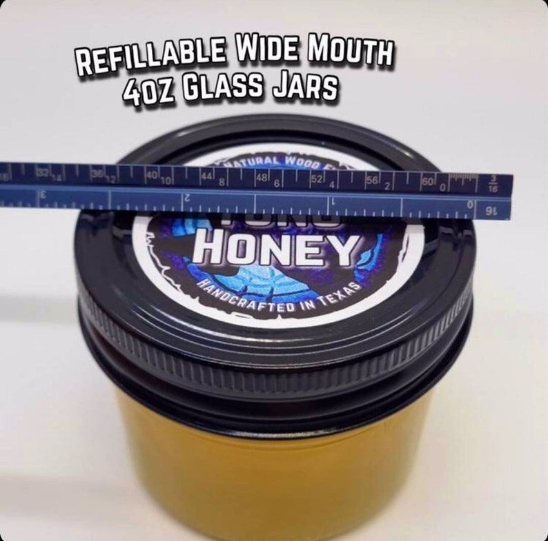 May include: A 4 ounce glass jar with a wide mouth, filled with honey. The jar has a black lid with a label that says "YUM HONEY" in blue and white text. The label also says "HANDCRAFTED IN TEXAS".