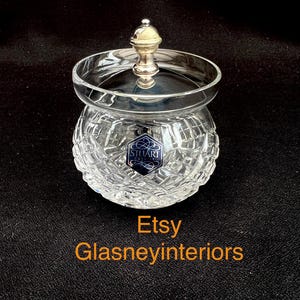 May include: A clear crystal jar with a silver lid and a diamond-cut pattern. The jar has a round shape and a small, decorative silver handle on top. The jar has a blue and white label that says "STUART". The text "Etsy Glasneyinteriors" is at the bottom.