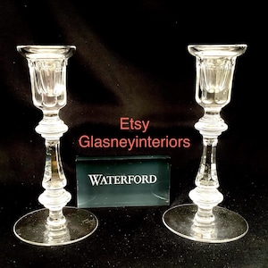 K&ouml;nnte beinhalten: Zwei klare Glas-Kerzenhalter mit einem Waterford-Etikett. Die Kerzenhalter haben ein geriffeltes Design und einen runden Sockel.