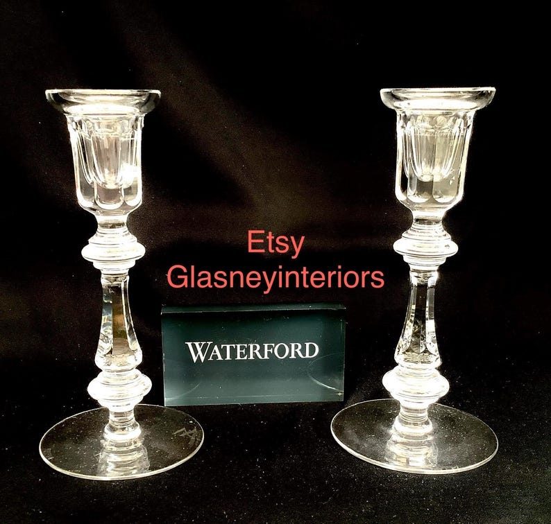 K&ouml;nnte beinhalten: Zwei klare Glas-Kerzenhalter mit einem Waterford-Etikett. Die Kerzenhalter haben ein geriffeltes Design und einen runden Sockel.