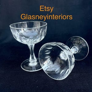 Könnte beinhalten: Zwei klare Sektgläser mit geätzten Mustern. Ein Glas steht aufrecht, das andere liegt auf der Seite. Die Gläser haben eine runde Schale und einen schlanken Stiel. Der Text "Etsy Glasneyinteriors" ist im Bild zu sehen.