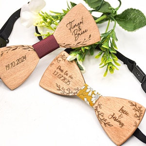 Może przedstawiać: Dwie drewniane muchy z grawerowanymi tekstami i wzorami kwiatowymi. Jedna ma bordowe centrum, druga żółte kwiatowe centrum. Teksty zawierają imiona i daty, takie jak "Florent & Brice" i "19.10.2024".