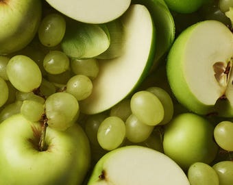 Puede incluir: Una selección de productos frescos verdes que incluye manzanas de color verde claro enteras y en rodajas junto a racimos de uvas de color verde pálido. La composición muestra texturas variadas de piel lisa, pulpa blanca y uvas redondas.