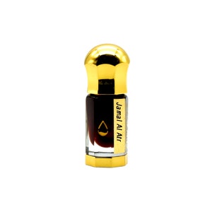 May include: A small perfume bottle with a gold cap and base. The bottle contains a dark, reddish-brown liquid. The label reads "Jamal Al Atr" with a droplet symbol. The bottle is set against a white background.