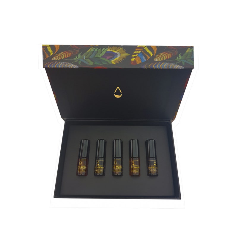 May include: An open black box with five small, dark glass bottles arranged in a row. The box lid features a colorful feather design. Each bottle has a black cap and a label with gold text.
