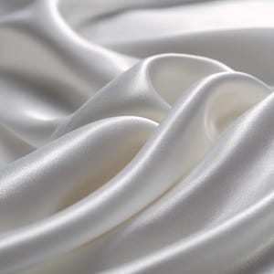 Può includere: Primo piano di tessuto di raso bianco con morbide pieghe e una lucentezza lucida. Il tessuto appare liscio e fluido, con luci e ombre che creano profondità. L'immagine mostra la consistenza e l'eleganza del materiale.