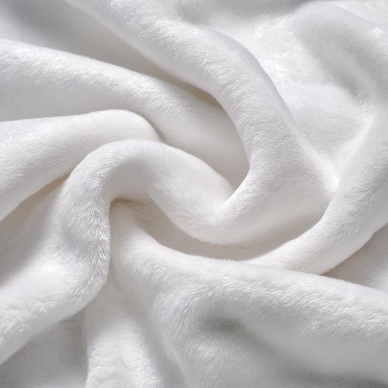 May include: Close-up of a soft, white, plush fabric with a velvety texture. The material is tightly woven, creating a smooth surface with gentle folds and curves. The fabric appears thick and luxurious, ideal for blankets or throws.