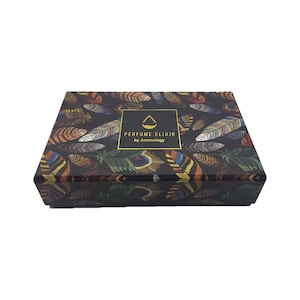 May include: A rectangular box with a black background and a pattern of colorful feathers. The box has a gold-framed label that reads "PERFUME ELIXIR by Aromology". The feathers are in shades of orange, yellow, green, and blue.