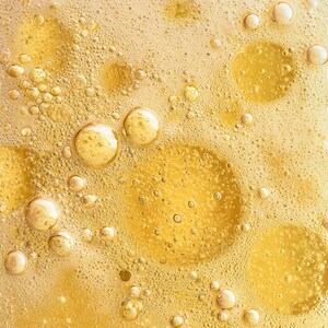 May include: Close-up of a golden liquid with numerous bubbles of varying sizes. The bubbles range from tiny specks to larger, spherical shapes, creating a textured, effervescent appearance. The overall effect is a warm, inviting, and abstract composition.