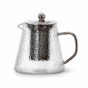 May include: A clear glass teapot with a textured surface and a stainless steel lid and handle. The teapot has a spout for pouring and a built-in infuser. The design is modern and minimalist, suitable for brewing tea.
