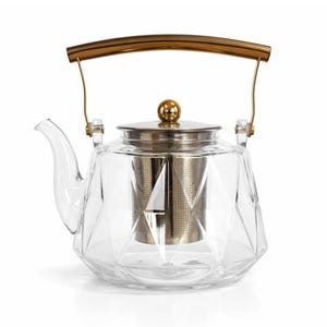 May include: A clear glass teapot with a geometric design. It features a gold-colored handle and lid, and a metal tea infuser inside. The teapot is designed for brewing tea.