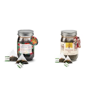 Puede incluir: Dos tarros de té de vidrio con tapas plateadas. Uno está etiquetado como "Winter Spiced Tea" y el otro como "Christmas Tea". Cada tarro tiene una etiqueta decorativa y varias bolsitas de té. Las bolsitas son blancas, triangulares y tienen etiquetas verdes.