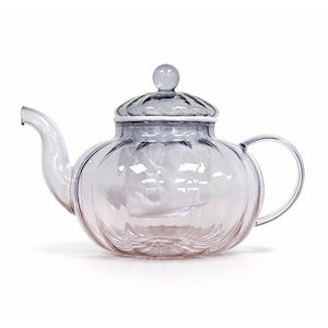 May include: A clear glass teapot with a rounded body and a lid. The teapot has a curved spout and a handle. The lid is topped with a small, round knob. The glass has a slight tint of blue and pink.