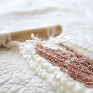 May include: A wall hanging made of white and pink yarn, with a wooden dowel at the top.