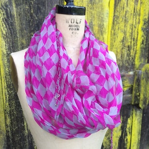 May include: A pink and grey patterned scarf with a diamond pattern. The scarf is draped around a mannequin's neck. The mannequin is wearing a black belt.