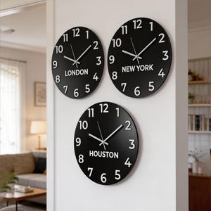 May include: Three circular wall clocks with black faces and white numerals. Each clock features white hour, minute, and second hands. The clocks are labeled with the city names LONDON, NEW YORK, and HOUSTON printed in white text below the center.