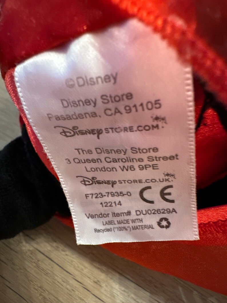 K&ouml;nnte beinhalten: Ein wei&szlig;es Etikett mit dem Disney-Logo und Store-Informationen aus Pasadena, CA, und London, UK. Das Etikett enth&auml;lt auch die Artikelnummer des Verk&auml;ufers und gibt an, dass es aus recyceltem Material hergestellt wurde.