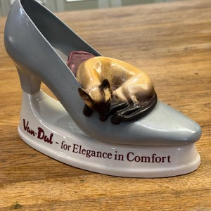 Puede incluir: Una taza de cerámica blanca con un asa negra y el texto "But First, Coffee" en negrita negra. La taza está sobre un fondo borroso. La taza mide aproximadamente 10 cm de altura.