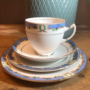 May include: A white teacup and saucer set with a blue and gold floral pattern. The teacup has a gold rim and the saucer has a gold band around the edge.